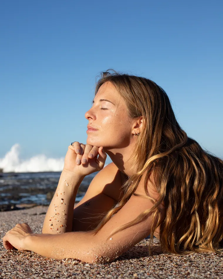 Charlotte lying on the sand with her eyes closed and the late sun on her face